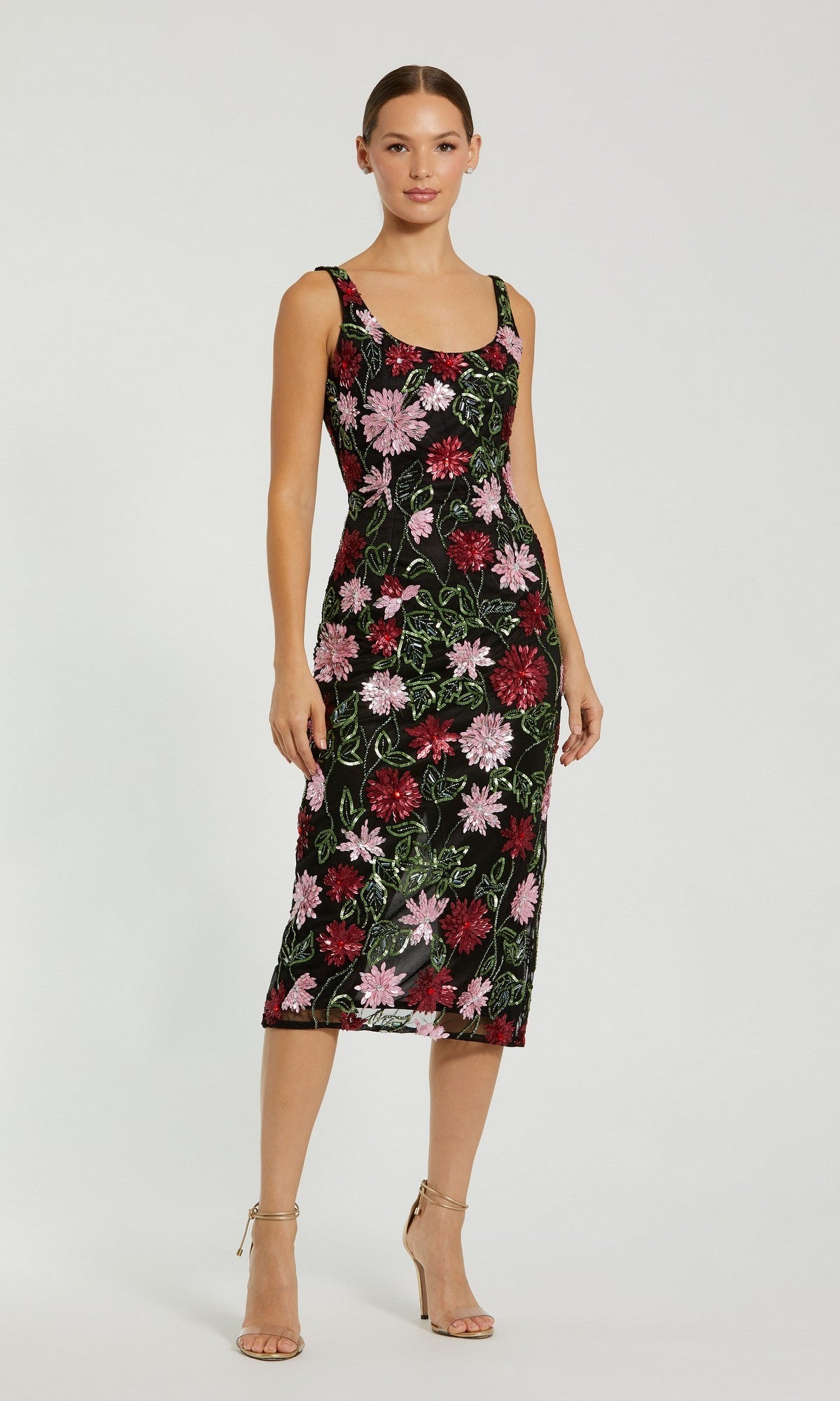 A woman stands in the Beaded Midi Wedding Guest Dress: Mac Duggal 6124, a sleeveless black knee-length dress with pink and red floral beading, paired with nude heels against a plain light background.